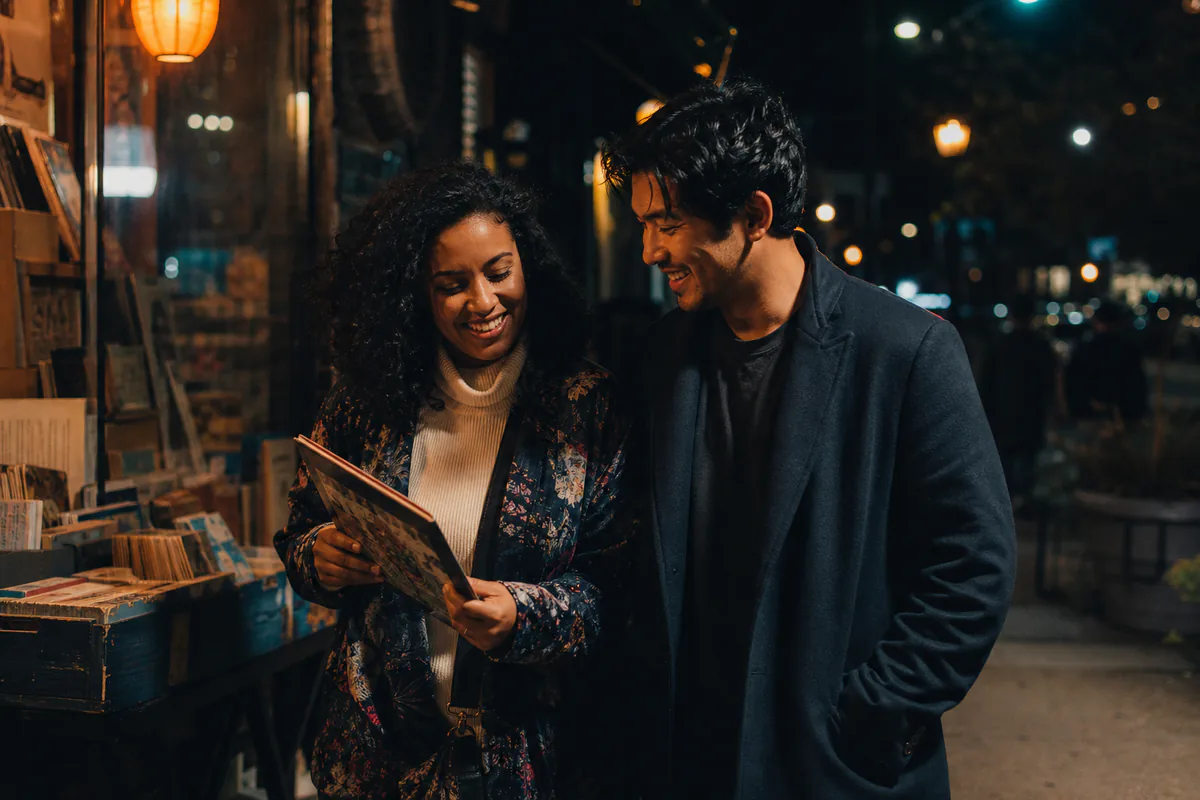 A couple laughs while browsing records at a nighttime street stall.